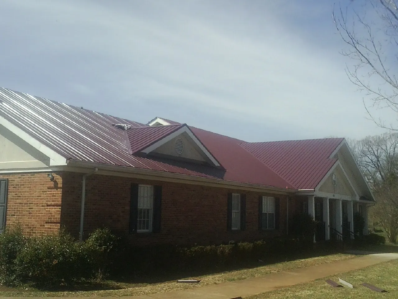 Red metal roof with gabled entries on a long brick building, from a Hail Damage Roof Repair job in Pleasantville
